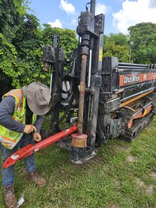Worker preparing a horizontal directional drilling (HDD) rig with a drill rod before underground utility installation at a construction site.