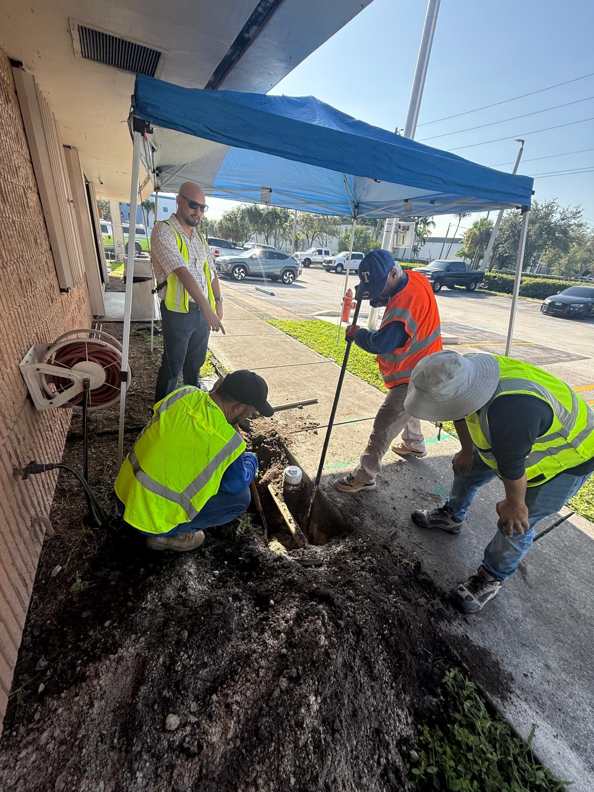 Utility crew excavating and inspecting an underground utility connection near a commercial building
