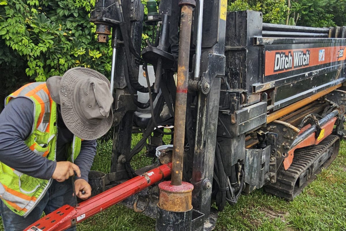 Worker preparing a horizontal directional drilling (HDD) rig with a drill rod before underground utility installation at a construction site.